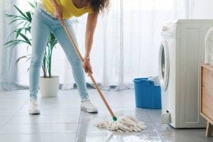Broken washing machine leaking on the floor, a woman is cleaning with a mop