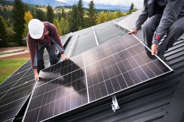 Builders building photovoltaic solar module station on roof of house. Men electricians in helmets installing solar panel system outdoors. Concept of alternative and renewable energy