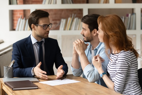 Professional male lawyer financial advisor consulting happy family couple clients in modern office. Interested young customers meeting realtor broker bank worker, discussing agreement or deal