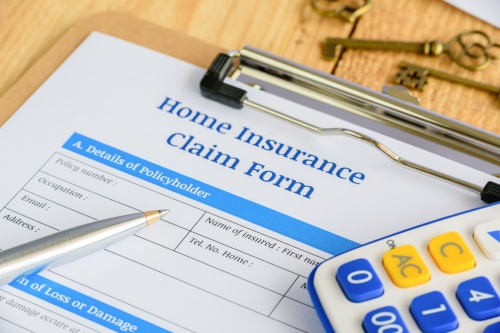 Blue ballpoint pen, two antique brass keys and a home insurance claim from on a plywood clipboard. A blank form is waiting to be completed and signed by a policyholder or an insured person.