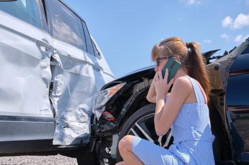 Sad female driver speaking on sellphone on street side calling for emergency service after car accident. Road safety and insurance concept