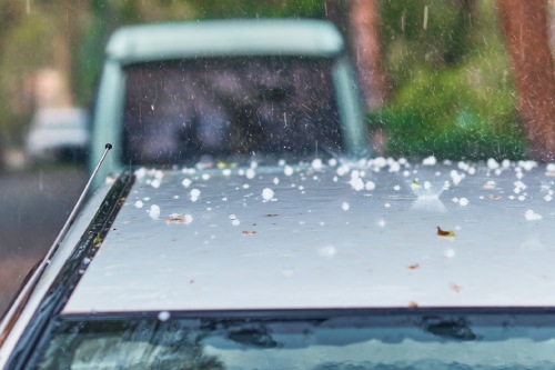 Hail and leaves from trees on the roof of a car in a heavy rain storm. A rare natural phenomenon. Texture of water splashes and ice fragments. Close up. Selective focus.