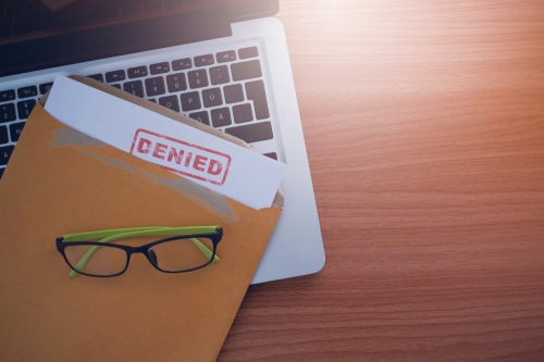 Document with denied stamp put on the laptop on wooden table,