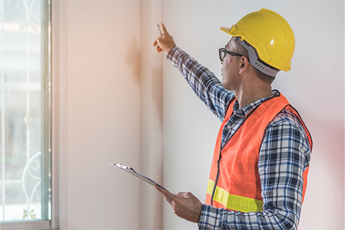 A construction worker in an orange vest and hard hat gestures towards a window, addressing storm damage concerns for residents.