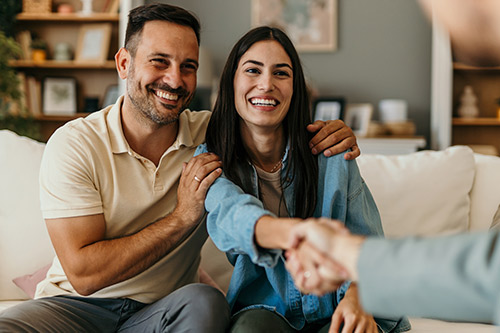 A real estate agent shakes hands with a man and woman, guiding them through property options after hurricane damage.