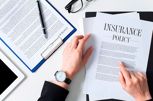 Desk with an insurance policy, laptop, and tablet, illustrating the topic of how insurers undervalue commercial claims.