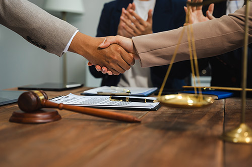 Two business people engaging in a handshake across a desk, representing collaboration on commercial claims issues.