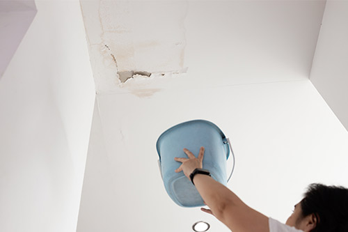 A woman holds a blue bucket in a white room, highlighting potential hidden issues after the recent storm in Boerne.