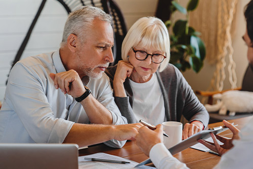 A man and woman look at a tablet, with an older man seated at a table, focusing on insurance issues from Texas hailstorms.