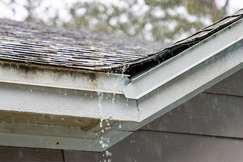 Water cascades from a roof into a gutter, highlighting the challenges of property damage claims in Texas during October.