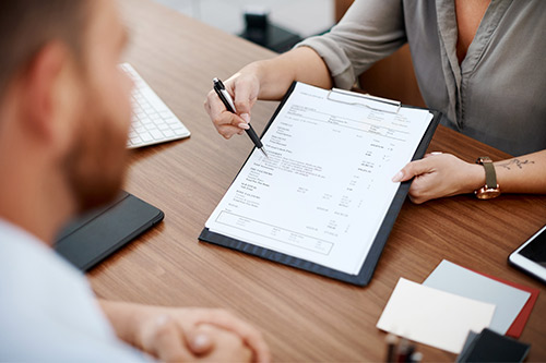 A man and woman review a business document together, discussing challenges of property damage settlements in Texas in October.