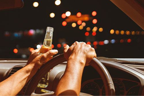 An individual grips a beer bottle while driving, emphasizing the risks of alcohol-related accidents during the holidays.