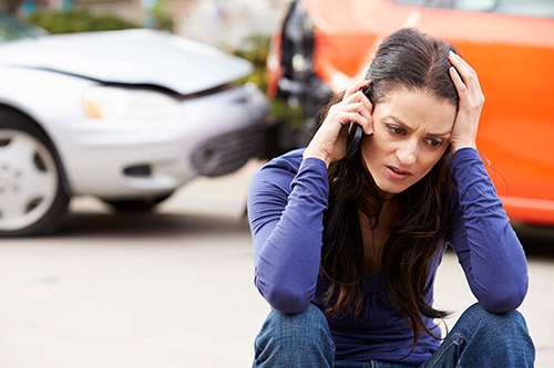 A woman sits on the ground beside a car with a shattered windshield, highlighting the impact of holiday season accidents.