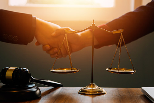 A lawyer and judge shake hands above scales of justice, representing commitment to families affected by wrongful death claims.