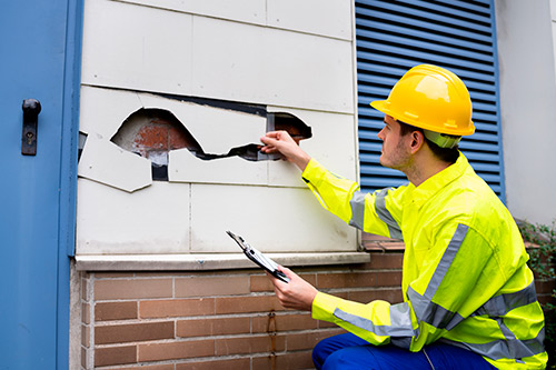 A construction worker in a hard hat and safety vest fixes a wall hole, representing home building in Harlingen, TX.