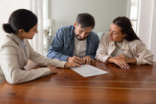 A couple and a man seated at a table, signing documents related to custom versus pre-built homes in Harlingen, TX.