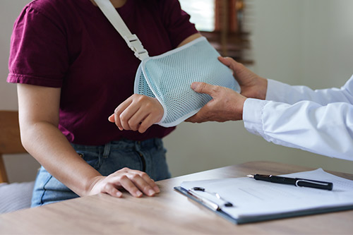 Un médico examina a una mujer con un brazo ortopédico, lo que indica que se centra en su reciente lesión.
