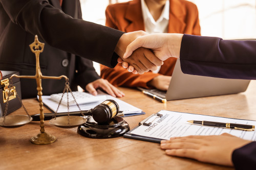  Two business people shake hands at a desk with a scale and laptop, representing collaboration in choosing a personal injury lawyer.