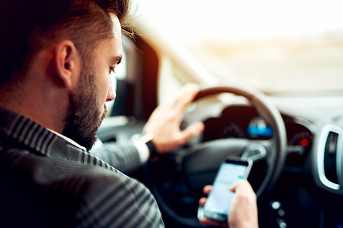 A man in a suit uses his cell phone while driving, illustrating the risks of distracted driving on Texas highways this Spring Break.