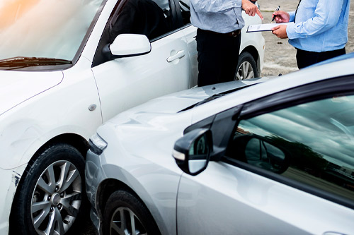Insurance agent writing on clipboard while examining car after accident claim being assessed and processed