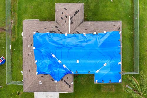Home rooftop wrapped in plastic tarp following hurricane damage, protecting structure from water penetration until permanent roofing materials are restored