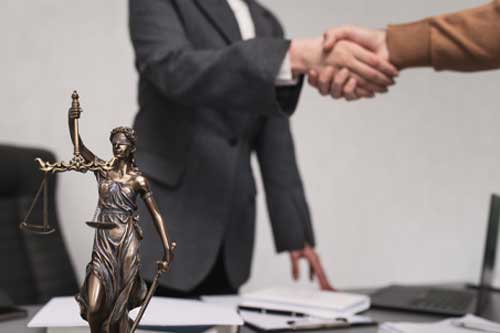Client shakes hands with lawyer, notary statue of Themis close-up on table in lawyer's office. Conclusion of deal, legislation