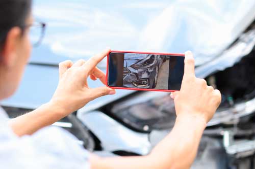 Woman agent takes pictures of damage to car after accident by smartphone