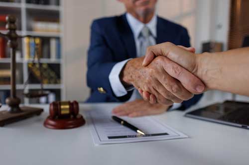 Happy mid aged business lawyer man manager handshaking greeting client in office. Smiling female executive making successful deal with partner shaking hand at work standing at meeting table.