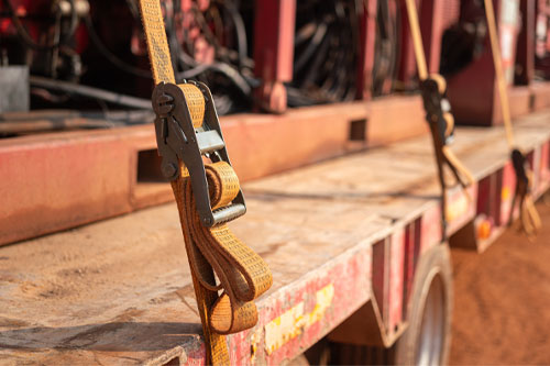 Latching belt strap with metal buckle that securing heavy load on trailer truck to prevent object falling during transportation. Close-up and selective focus.