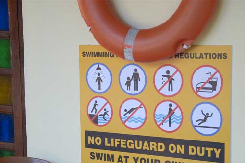 Swimming Pool Regulations Sign with Safety Icons and Lifebuoy on Wall