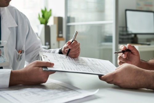 Middle aged Caucasian male patient consulting with doctor in medical office, both reviewing medical records and filling out health forms during diabetes management appointment