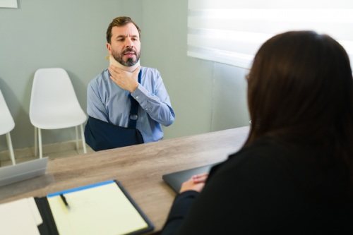 Injured man with neck brace and arm sling explaining his accident to an insurance agent in an office setting
