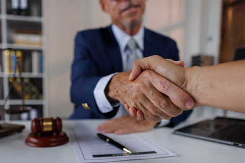 Happy mid aged business lawyer man manager handshaking greeting client in office. Smiling female executive making successful deal with partner shaking hand at work standing at meeting table.